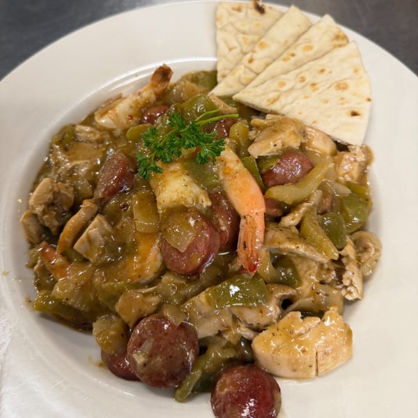 Hearty Cajun gumbo with shrimp, chicken, sausage, and bell peppers, served with pita bread.
