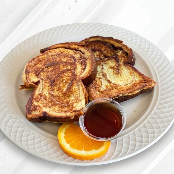 Golden brown French toast slices with a side of syrup and an orange wedge on a white plate.
