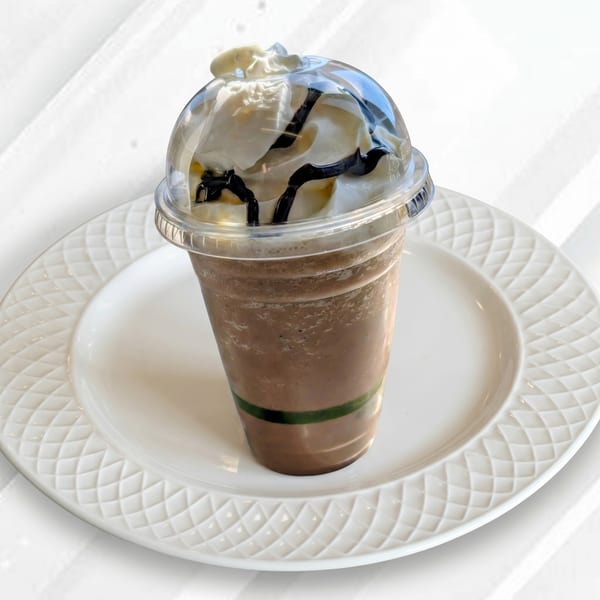 Chocolate frappe with whipped cream and chocolate drizzle in a plastic cup on a white plate.