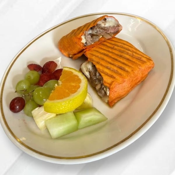 A golden-brown panini with meat and cheese filling, served with a side of fresh fruit.