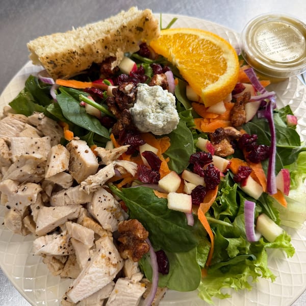 Chicken salad with cranberries, apples, walnuts, blue cheese, orange slice, and bread.