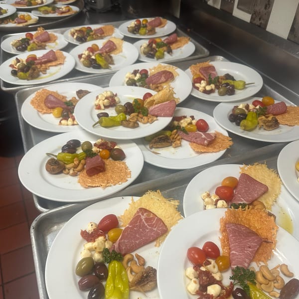 Multiple plates of appetizers with cured meat, cheese crisps, tomatoes, olives, and nuts on a tray.