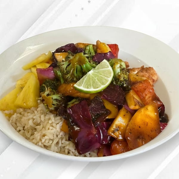 A white bowl filled with rice, pineapple, and stir-fried vegetables with a lime wedge.