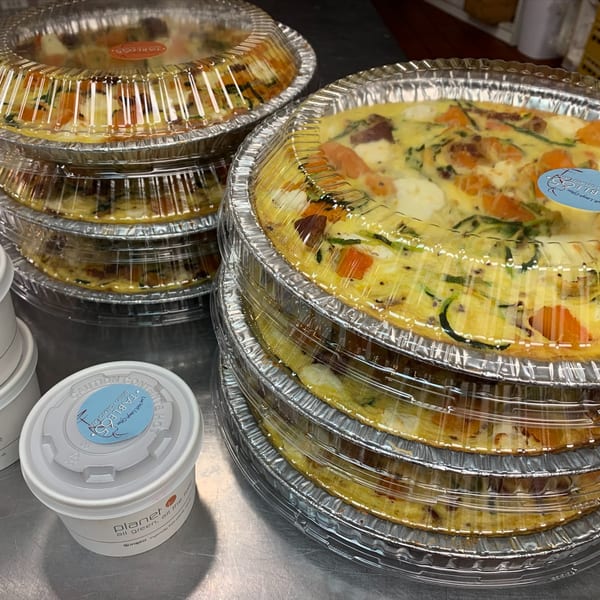 Stacks of quiches in foil pans with clear lids, alongside a white container from "Table 05".