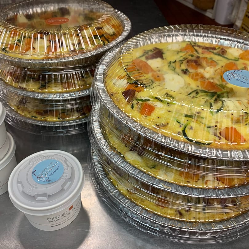 Stacks of quiches in foil pans with clear lids, alongside a white container from "Table 05".