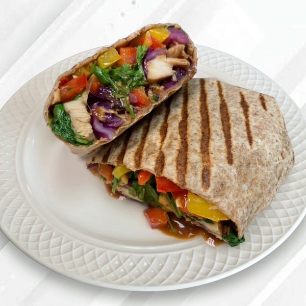 Grilled chicken and vegetable wrap, cut in half, on a white plate.