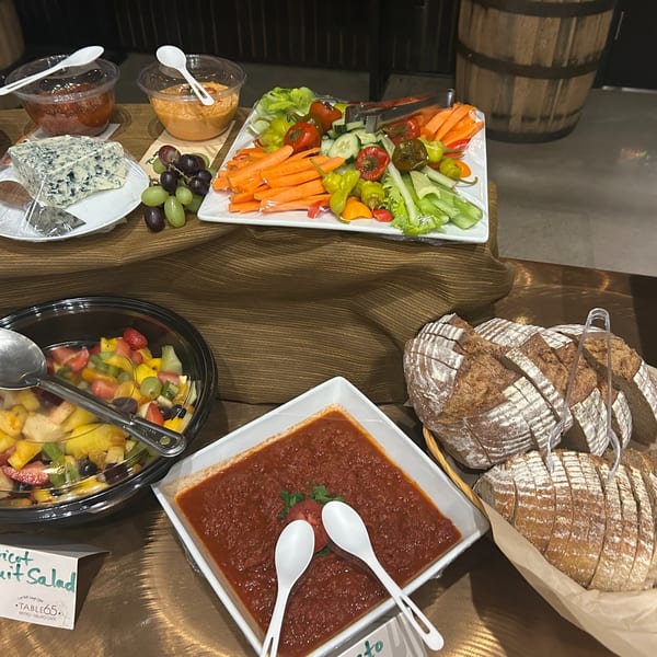 A buffet spread with fruit salad, vegetable platter, cheese, dips, tomato sauce, and sliced bread.