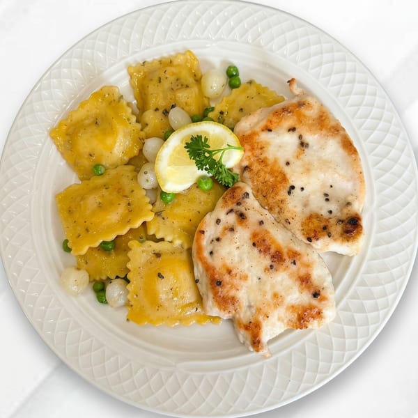 Grilled chicken with ravioli, peas, pearl onions, and a lemon wedge on a white plate.